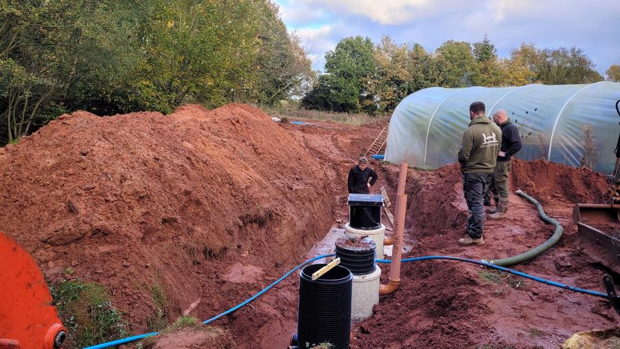 Chantier d'assainissement : tranchée ouverte, regards et canalisations en cours de pose dans un jardin